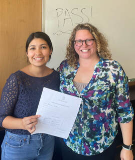 Rebecca Revilla, smiling, holding paperwork that indicates she passed her comprehensive exam with Dr. Caitlin Hudac (also smiling).